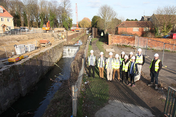 A group of people wearing hard hats and high visibility jackets pose for a photograph next to the lock before completion of restoration work.
