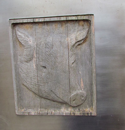 A wooden plaque showing a carving of a pig's head.