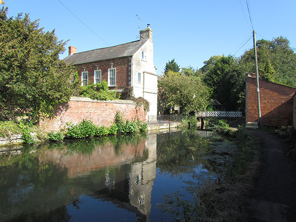 A Georgain house with a tall red brick wall sits right next to the waterway wall. Ryeford swing bridge is in the background.