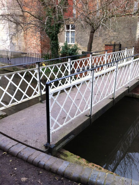 A bridge with crossed decorative metal, painted black and white, leads across the canal.