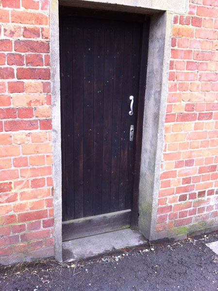 A small, black painted door in a red brick wall.