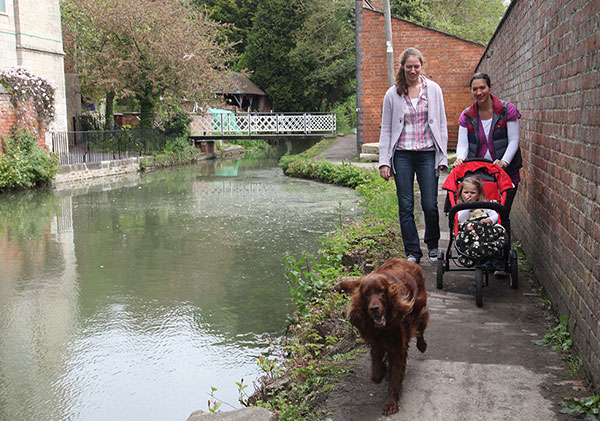 Two young women walk with a pushchair and red setter dog on the towpath with Ryeford Swing Bridge  in the background