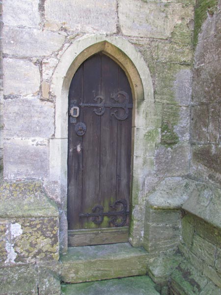 Small wooden door with massive iron hinges and latch and simple carved stone surround.